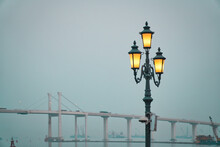 Old Beautiful Illuminated Street Lamp In Macau Fisherman's Wharf With A Bridge In The Background