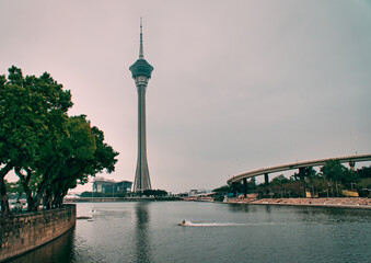 Poster - Scenic view of the Macau Tower with green trees and a river on a blue cloudy sky background