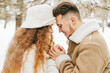 © klavdiyav - young couple in love man and woman in fashion stylish winter clothes standing in snowy pine forest and having fun spending time together, concept of valentine's day and newlyweds, tenderness and love