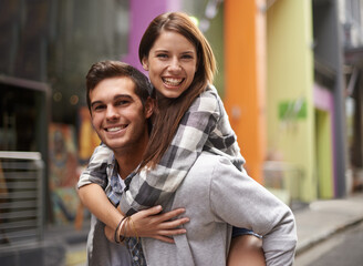 Sticker - Totally in love. A young guy smiling while piggybacking his girlfriend out in the street.