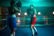 Serious girls exercising boxing together in gym. Two trained girls in sportswear preparing for boxing match instructing each other new punches and defense. Healthy lifestyle and sport activity concept