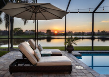 Florida Screened Swimming Pool With Lounge Chairs Overlooking Lake At Sunset