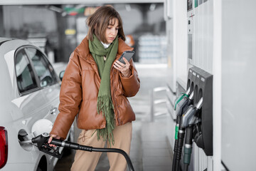 woman refueling car with gasoline, using smartphone to pay. concept of mobile technology for fast re