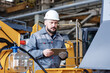 © pressmaster - Mature serious engineer or quality control manager of industrial plant with tablet standing in front of huge industrial machine