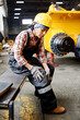 © pressmaster - Young female engineer in protective helmet and coveralls sitting on bench and touching her injured knee after accident at work