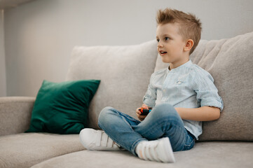 Happy boy playing video games holding game controller sitting on the coach in living room