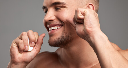 Floss like a boss. Studio shot of a handsome young man flossing his teeth against a grey background.