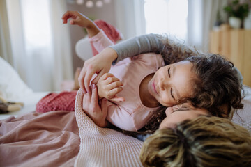 Wall Mural - Happy mother with her little daughter hugging and having fun together on bed at home.