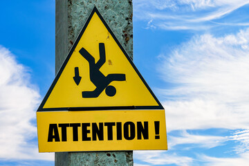 Yellow Attention sign with a falling man hanging on a pole, blue sky background with copy space