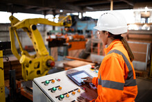 Female Industrial Worker In Safety Uniform And Hard Hat Operating Manufacturing Machine Via Control Panel.