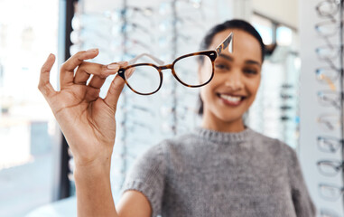 raise your glasses to good eye health. shot of a young woman buying a new pair of glasses at an opto