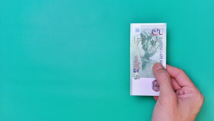 Singapore Dollar is the official currency of Singapore. Business Investment Economy Money Income Loan and Finance concept. Businessman's hand showing Singapore Dollar on a green background. 5 Five SGD