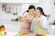 mother cutting fresh peppers on wooden cutting board with down syndrome teenage girl or her daughter in the kitchen
