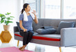 © Bangkok Click Studio - Asian young pretty happy healthy female athlete sport girl in casual sporty outfit sitting on sofa holding drinking bottle of water relaxing resting after learning exercising online in living room