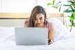 © Bangkok Click Studio - Asian young happy cheerful beautiful female model in casual pajama outfit lying down smiling hold credit card on bed in bedroom browsing surfing internet shopping online via laptop notebook computer