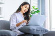 © Bangkok Click Studio - Asian young beautiful happy professional successful female businesswoman in casual outfit sitting on sofa smiling remotely working online during quarantine at home via laptop computer in living room