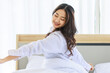 © Bangkok Click Studio - Asian young beautiful happy sexy female teenager model in casual pajama outfit waking up in morning sitting under white blanket on bed in bedroom holding hands spreading long hair relaxing refreshing