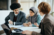 Young Muslim woman and her husband analyzing paperwork during meeting with their insurance agent.