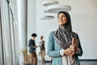 © Drazen - Smiling Muslim businesswoman standing in hallway at corporate office and looking through the window.