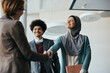 © Drazen - Happy Muslim businesswoman shaking hands with female colleague in hallway of an office building.