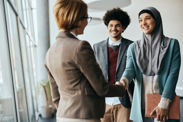 Young Muslim business people shaking hands with Caucasian CEO at corporate office.