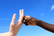A White-skinned Hand And A Black-skinned In Front Of A Blue Sky