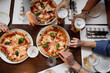 © Pintau Studio - Top view table with unrecognizable multiracial group of people's hands grabbing a slice of delicious Italian pizza and glasses of beer.