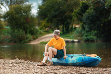 Outdoor Activities. A Young Woman Is Sitting On A Kayak And Scratching Her Leg From A Mosquito Bite. Camping Concept