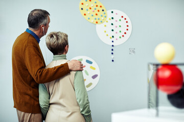 Rear view of senior man and woman in love having audio tour at exhibition in contemporary art museum