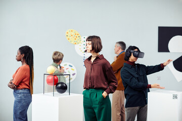 Group of diverse multi-ethnic young and senior people looking at contemporary art objects at exhibition in modern gallery