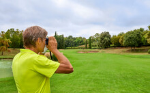 The Golfer Accurately Measures The Distance To The Flag In A Golf Course With The Laser Rangefinder. In The Background The Forest.