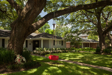 Red tire swing hanging from a tree at the detached residential house garden in Afton Oaks, Houston 