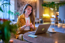 Happy Joyful Smiling Casual Satisfied Woman Learning And Communicates In Sign Language Online Using Laptop At Cafe
