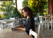 © Dragosh - Profile portrait of the beautiful young woman sitting at the table typing on the laptop at the terrace.