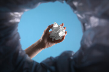 Bottom view of woman throwing crumpled paper into trash bin on light blue background, closeup