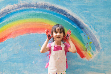 Asian little girl is painting the colorful rainbow and sky on the wall and she look happy and funny, concept of art education and learn through play activity for kid development.