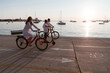 © .shock - Happy family enjoying a beautiful morning by the sea together, parents riding a bike and their son riding an electric scooter. Selective focus