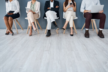 Whos going to be called up next. Closeup shot of a group of unrecognisable businesspeople using digital devices while sitting in line against a grey background.