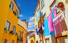 Lisbon, Portugal. Antique Alfama District With Coloured Houses On Background Of Blue Sky With Clouds. Washed Linen Dry On Ropes On Streets Between Building. Decorative Street Lamp On The Wall.