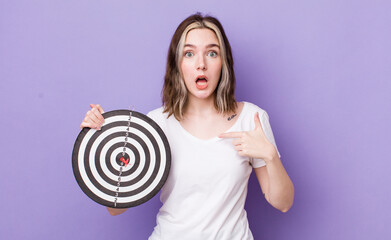 Wall Mural - pretty caucasian woman looking shocked and surprised with mouth wide open, pointing to self. dart target concept