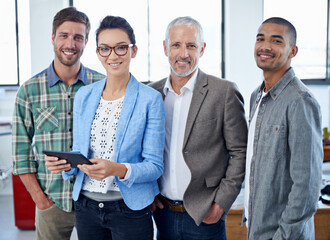 Wall Mural - The number one creative team. Portrait of a group of colleagues using a digital tablet while standing in an office.