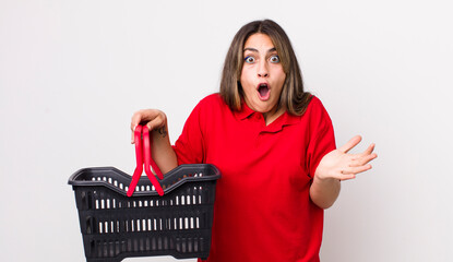 Wall Mural - pretty hispanic woman feeling extremely shocked and surprised. empty shopping basket concept