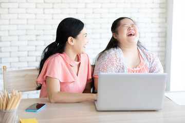 young teenage girl with down syndrome and her teacher using laptop computer together on a table