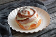 Cinnamon bun with cream on a white plate. Grey wooden background.