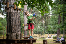 Strong Excited Young Boy Playing Outdoors In Rope Park. Caucasian Child Dressed In Casual Clothes And Sneakers At Warm Sunny Day. Active Leisure Time With Children Concept
