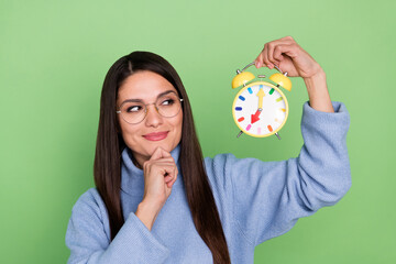 Poster - Photo of thinking young brunette lady look clock wear blue pullover eyewear isolated on green color background