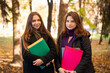 © Vitalii - Two cheerful students in Autumn park. Portrait of friends during the break, looking to the camera