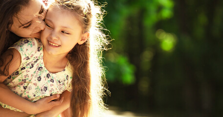 Wall Mural - Happy enjoying mother hugging her relaxing laughing kid girl on bright summer green trees background. Closeup family