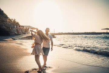 Wall Mural - A couple in love is walking on the beach near the sea. Young family at sunset by the mediterranean sea. Summer vacation concept