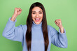 Photo of charming lucky young woman wear blue sweater smiling rising fists isolated green color background